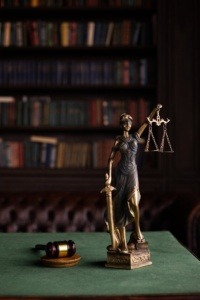 Statue of lady law with her sword and weight, on a table in front of a bookshelf.